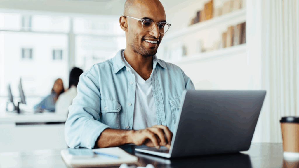 Set up a store A smiling man wearing glasses works on a laptop, searching for how to start a print-on-demand business.